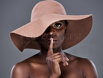 Buy stock photo Shot of a young woman wearing a hat and posing with her finger on her lips against a grey background