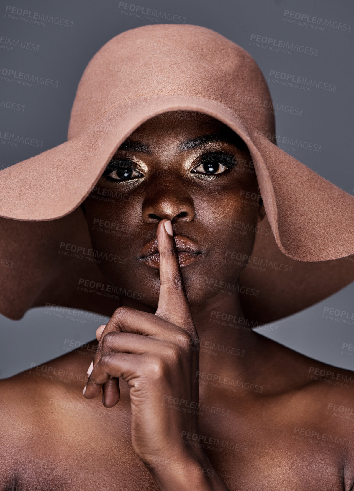 Buy stock photo Shot of a young woman wearing a hat and posing with her finger on her lips against a grey background