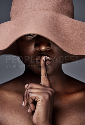 Buy stock photo Shot of a young woman wearing a hat and posing with her finger on her lips against a grey background