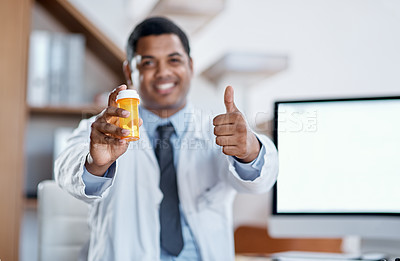 Buy stock photo Portrait of a young doctor holding a bottle of pills and showing thumbs up in his office