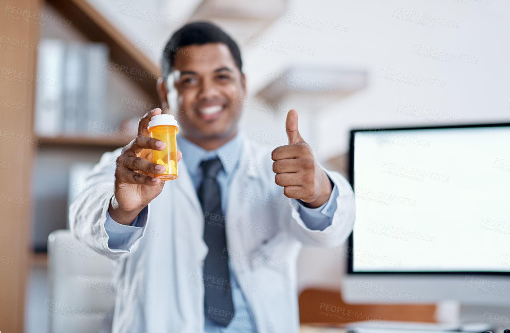 Buy stock photo Portrait of a young doctor holding a bottle of pills and showing thumbs up in his office