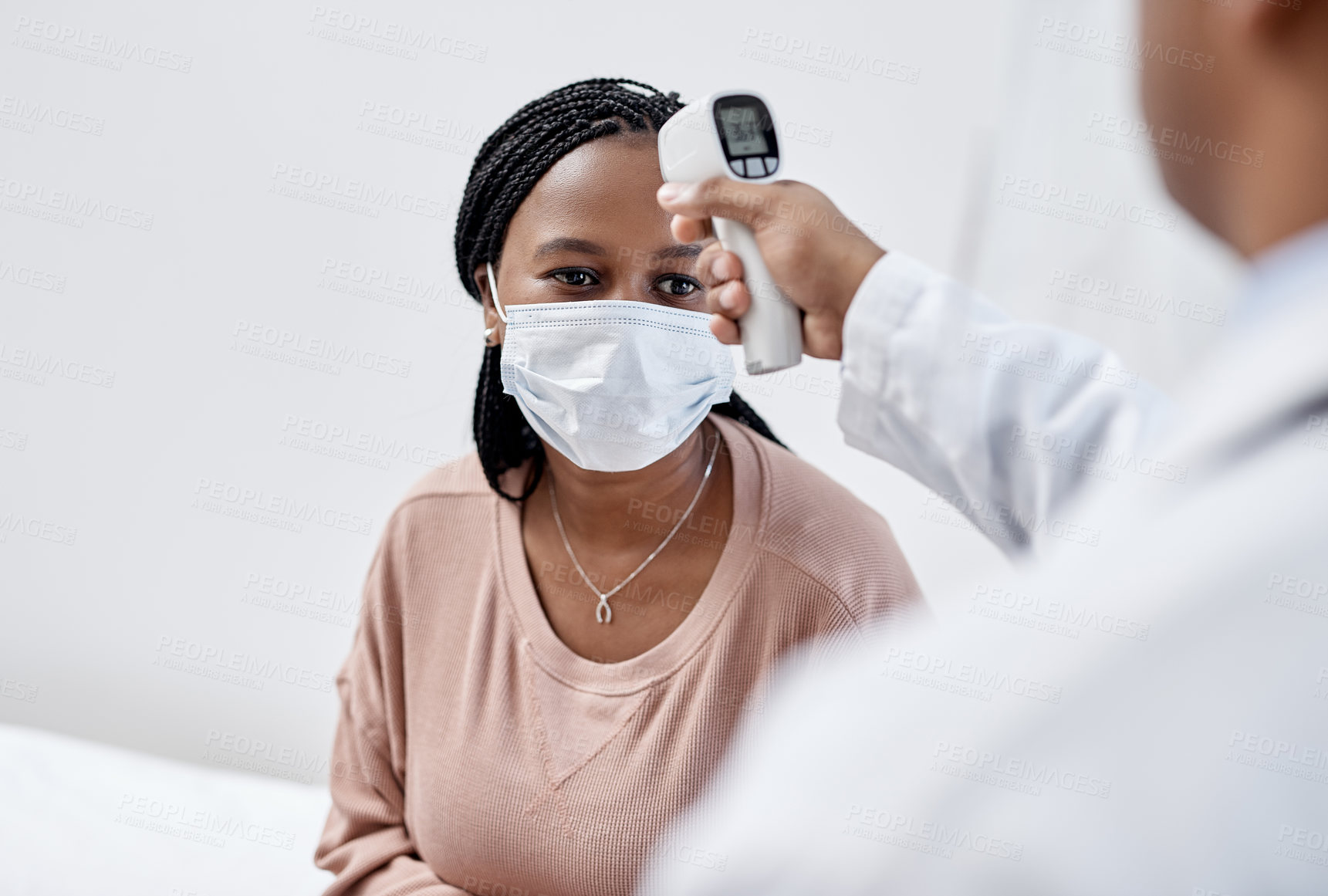 Buy stock photo Shot of a young woman getting her temperature taken with an infrared thermometer by a doctor