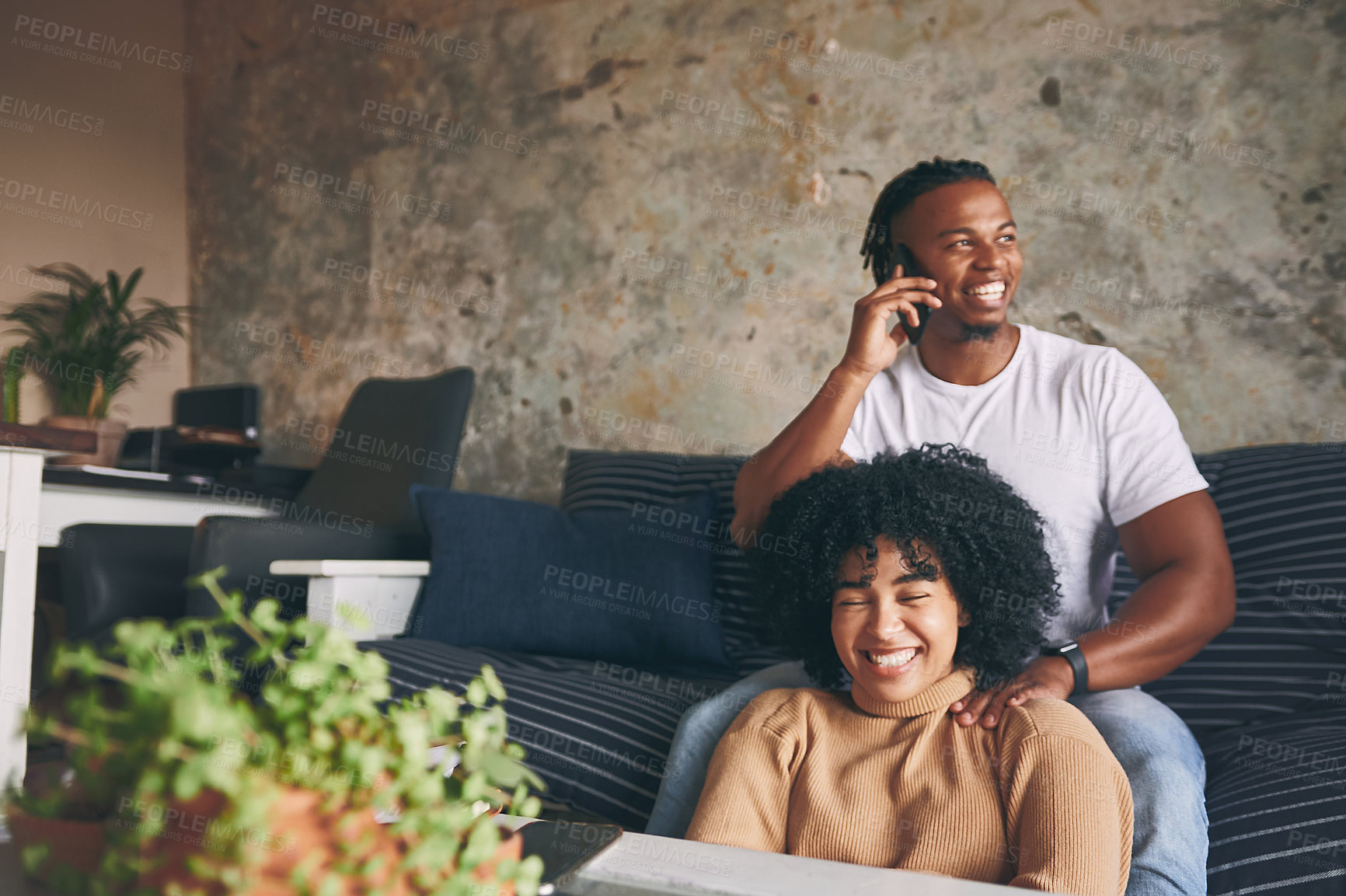 Buy stock photo Shot of a young man talking on a cellphone while relaxing with his girlfriend at home