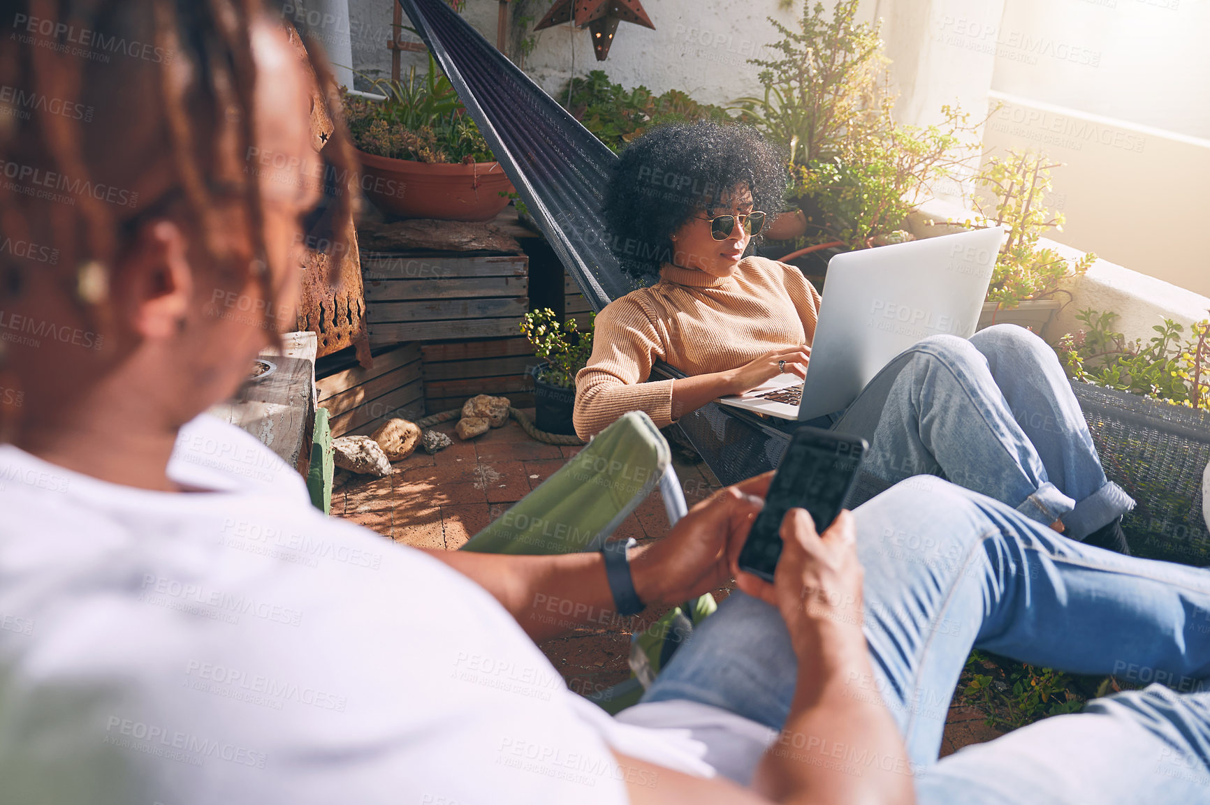 Buy stock photo Shot of a young woman using a laptop and relaxing on a hammock while her boyfriend uses a cellphone