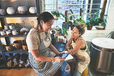 Buy stock photo Shot of two young women using a digital tablet while working together in a pottery studio