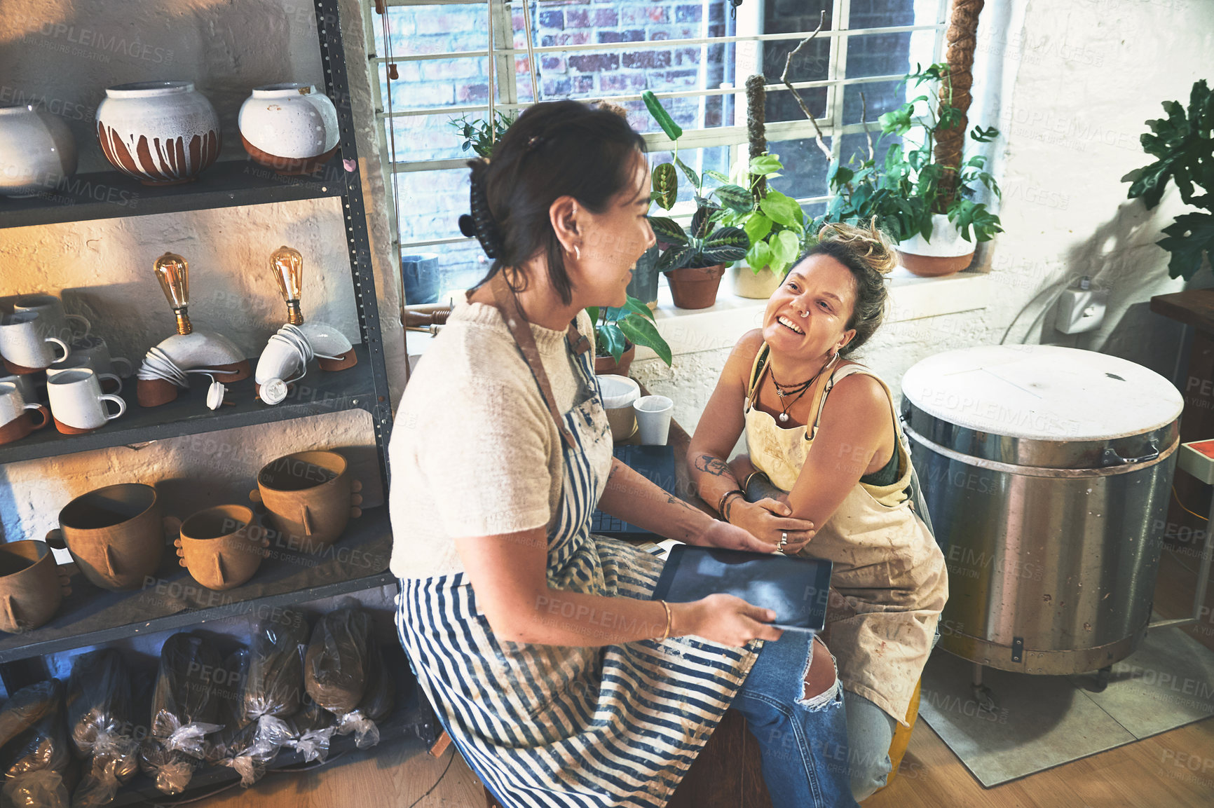 Buy stock photo Shot of two young women using a digital tablet during a meeting in a pottery studio