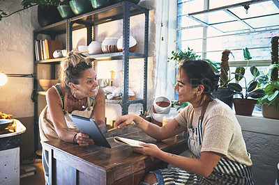 Buy stock photo Shot of two young women using a digital tablet during a meeting in a pottery studio