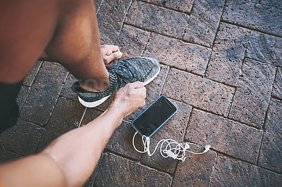 Buy stock photo Cropped shot of a man tying his shoelaces during a workout against an urban background