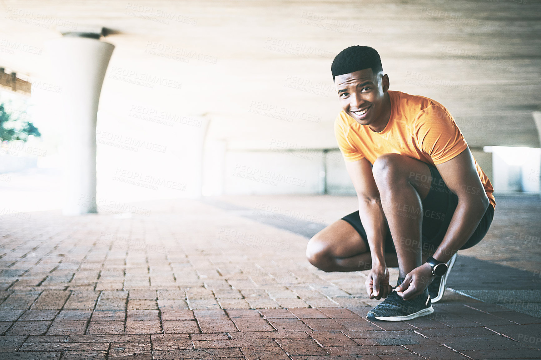 Buy stock photo Portrait of a young man tying his shoelaces during a workout against an urban background