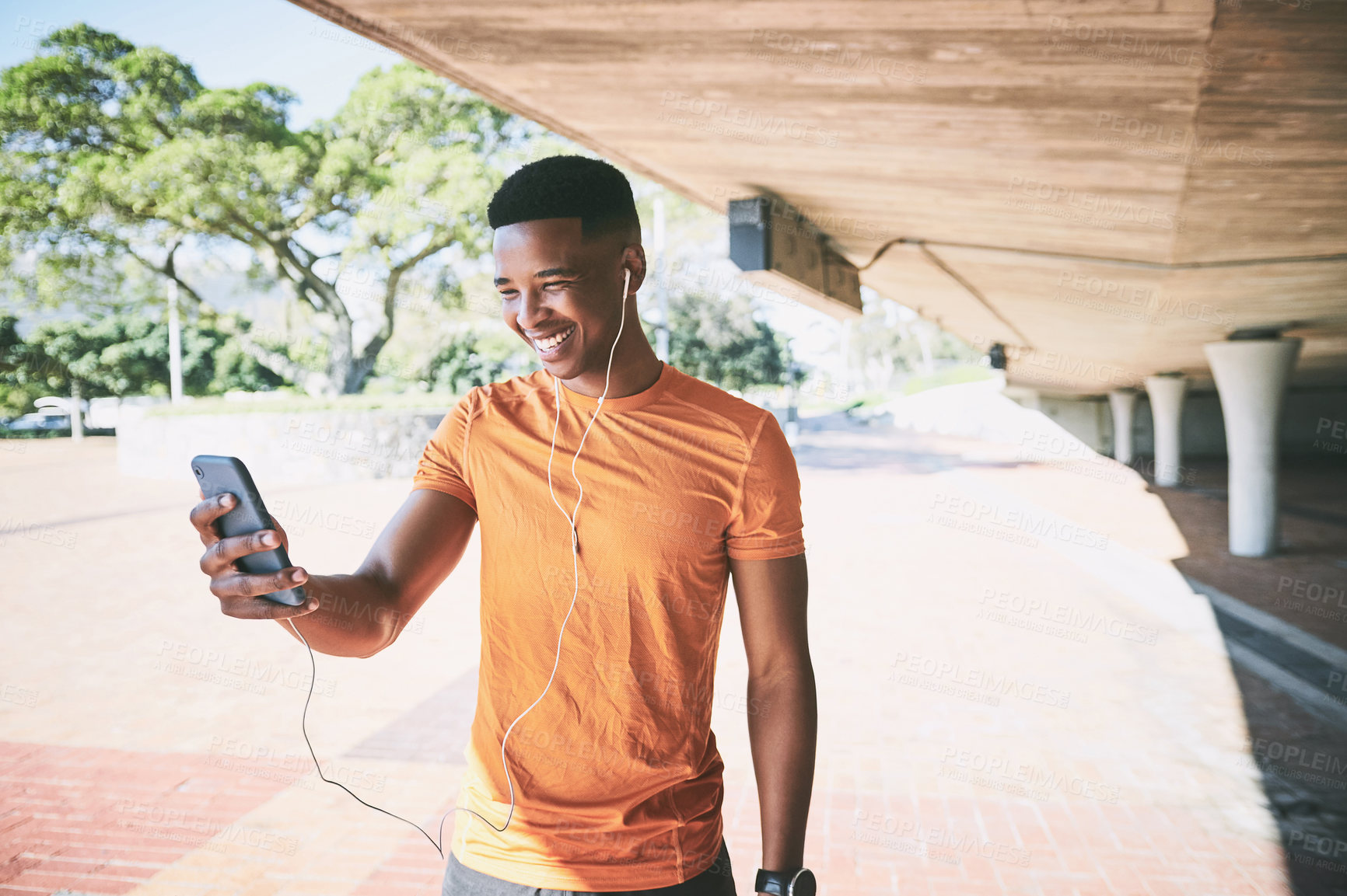 Buy stock photo Shot of a young man using a smartphone and earphones during a workout against an urban background