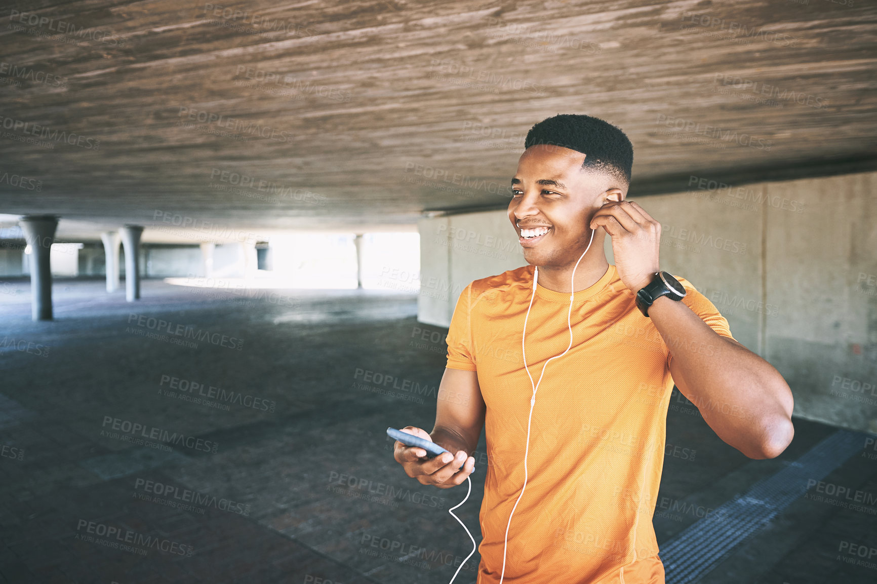 Buy stock photo Shot of a young man using a smartphone and earphones during a workout against an urban background