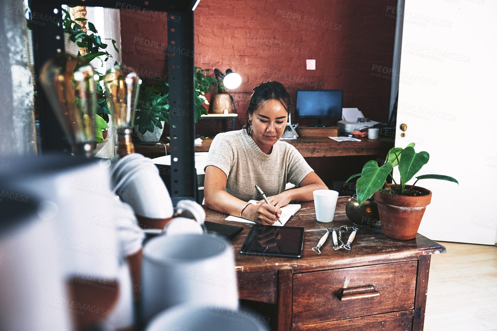 Buy stock photo Cropped shot of an attractive young business owner sitting alone in her pottery studio and making notes