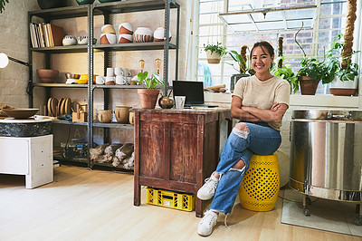 Buy stock photo Full length portrait of an attractive young business owner sitting alone in her pottery studio with her arms folded