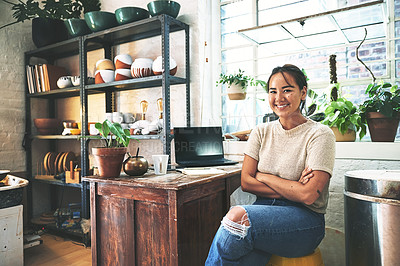Buy stock photo Cropped portrait of an attractive young business owner sitting alone in her pottery studio with her arms folded