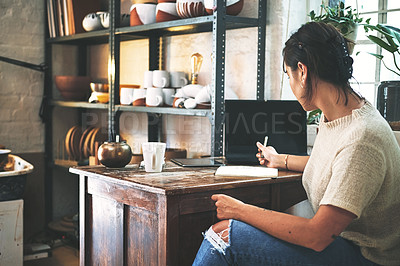 Buy stock photo Cropped shot of an unrecognizable business owner sitting alone in her pottery studio and making notes