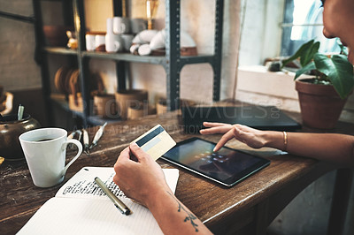 Buy stock photo Cropped shot of an unrecognizable business owner sitting alone in her studio and using a tablet for online shopping