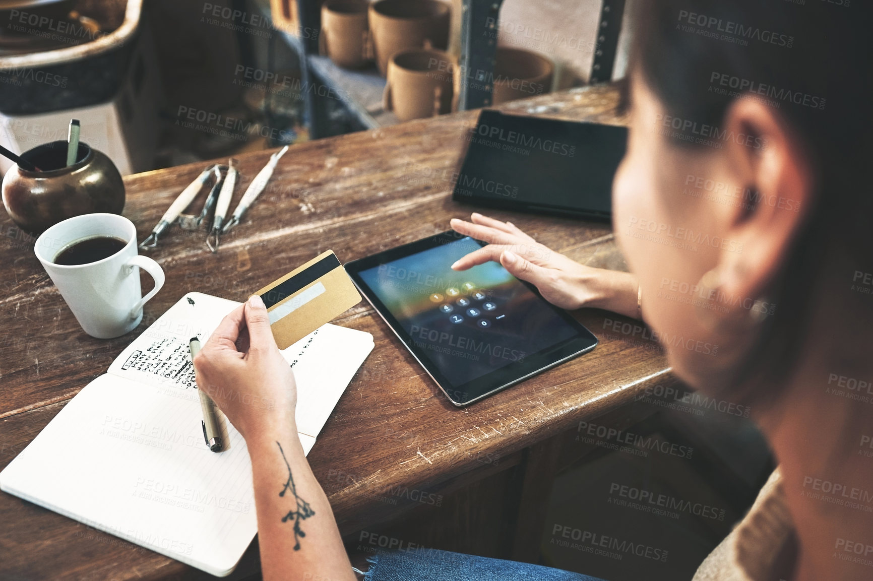 Buy stock photo Cropped shot of an unrecognizable business owner sitting alone in her studio and using a tablet for online shopping