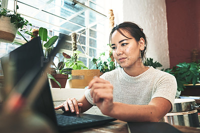 Buy stock photo Cropped shot of an attractive young business owner sitting alone in her studio and using a laptop for online shopping