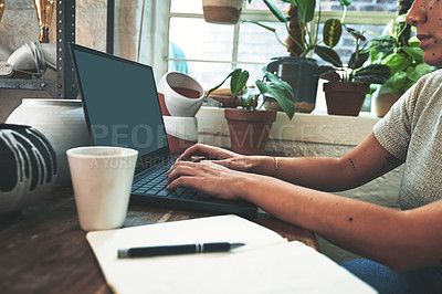 Buy stock photo Cropped shot of an unrecognizable business owner sitting alone in her pottery studio and using her laptop