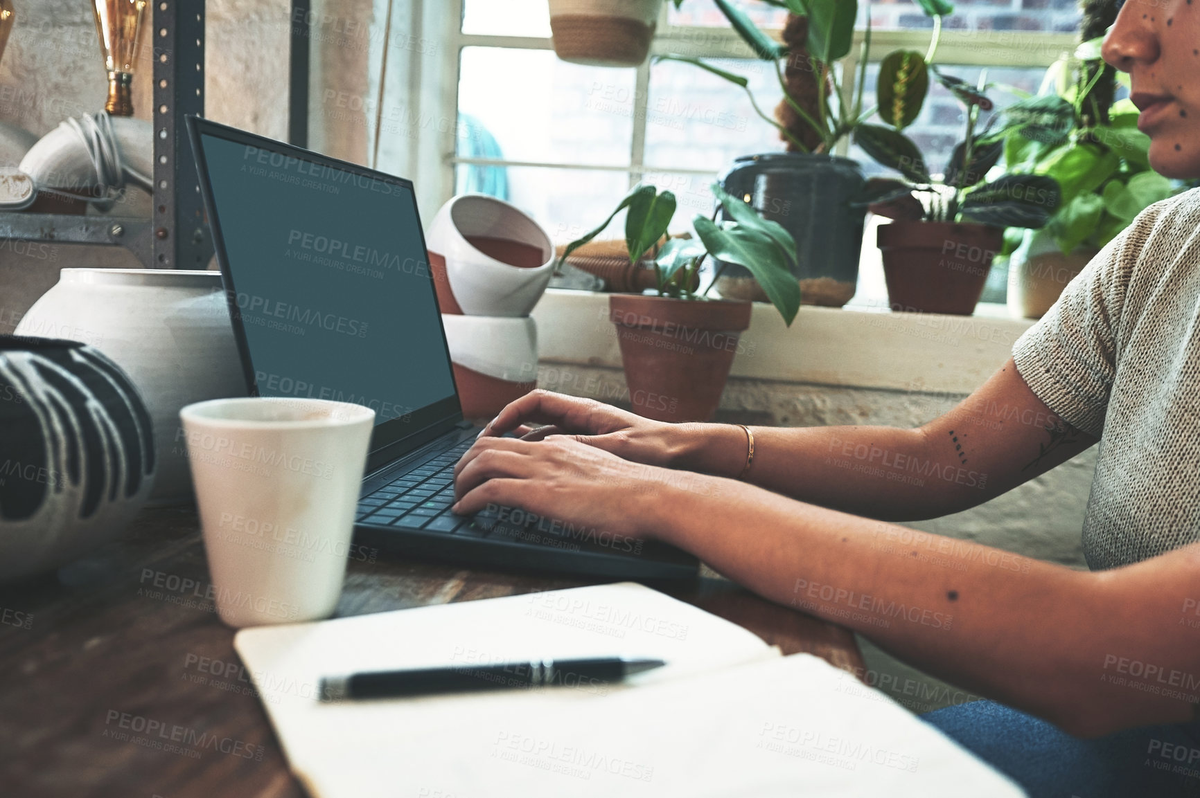 Buy stock photo Cropped shot of an unrecognizable business owner sitting alone in her pottery studio and using her laptop