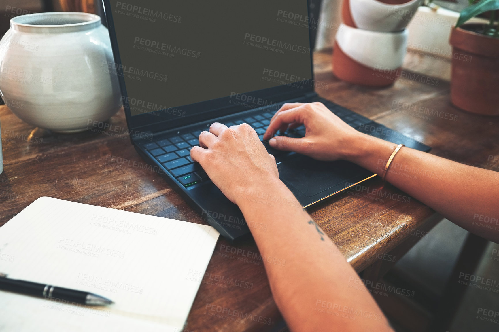 Buy stock photo Cropped shot of an unrecognizable business owner sitting alone in her pottery studio and using her laptop