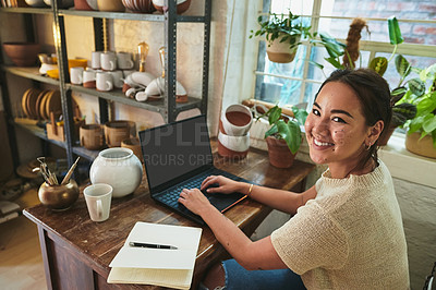 Buy stock photo Cropped portrait of an attractive young business owner sitting alone in her pottery studio and using her laptop