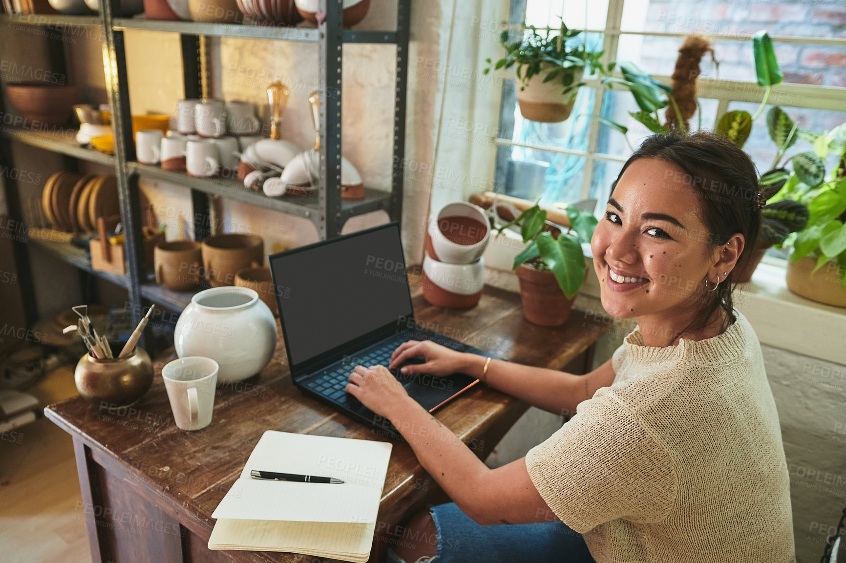 Buy stock photo Cropped portrait of an attractive young business owner sitting alone in her pottery studio and using her laptop