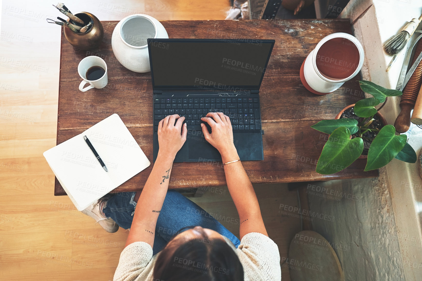 Buy stock photo High angle shot of an unrecognizable business owner sitting alone in her pottery studio and using her laptop