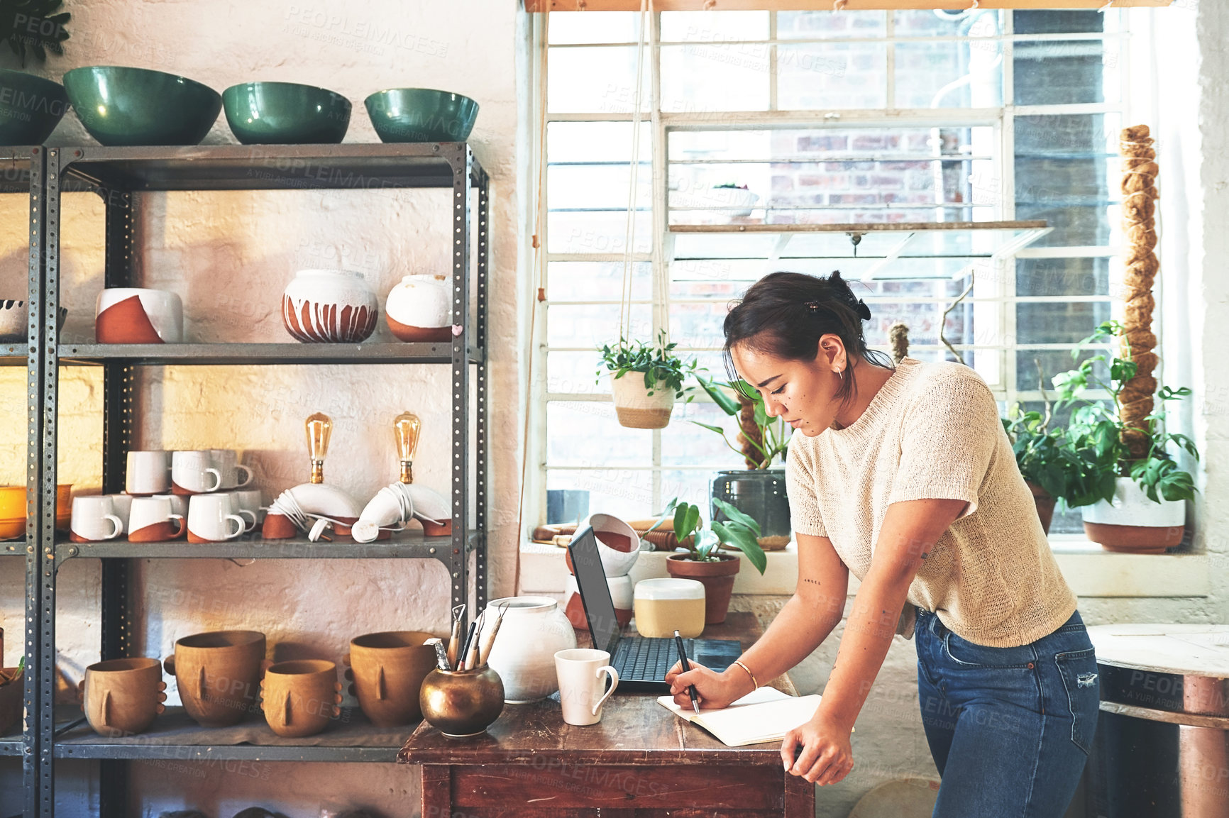 Buy stock photo Cropped shot of an attractive young business owner standing alone in her pottery studio and making notes