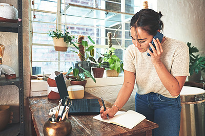 Buy stock photo Cropped shot of an attractive young business owner standing and using her cellphone while taking notes in her pottery studio