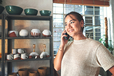 Buy stock photo Cropped shot of an attractive young business owner standing alone in her pottery studio and using her cellphone