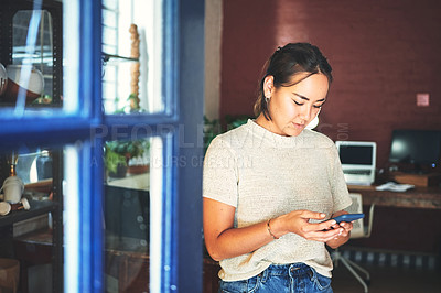 Buy stock photo Cropped shot of an attractive young business owner standing alone in her pottery studio and using her cellphone