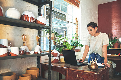 Buy stock photo Cropped shot of an attractive young business owner standing and using her laptop in her pottery studio