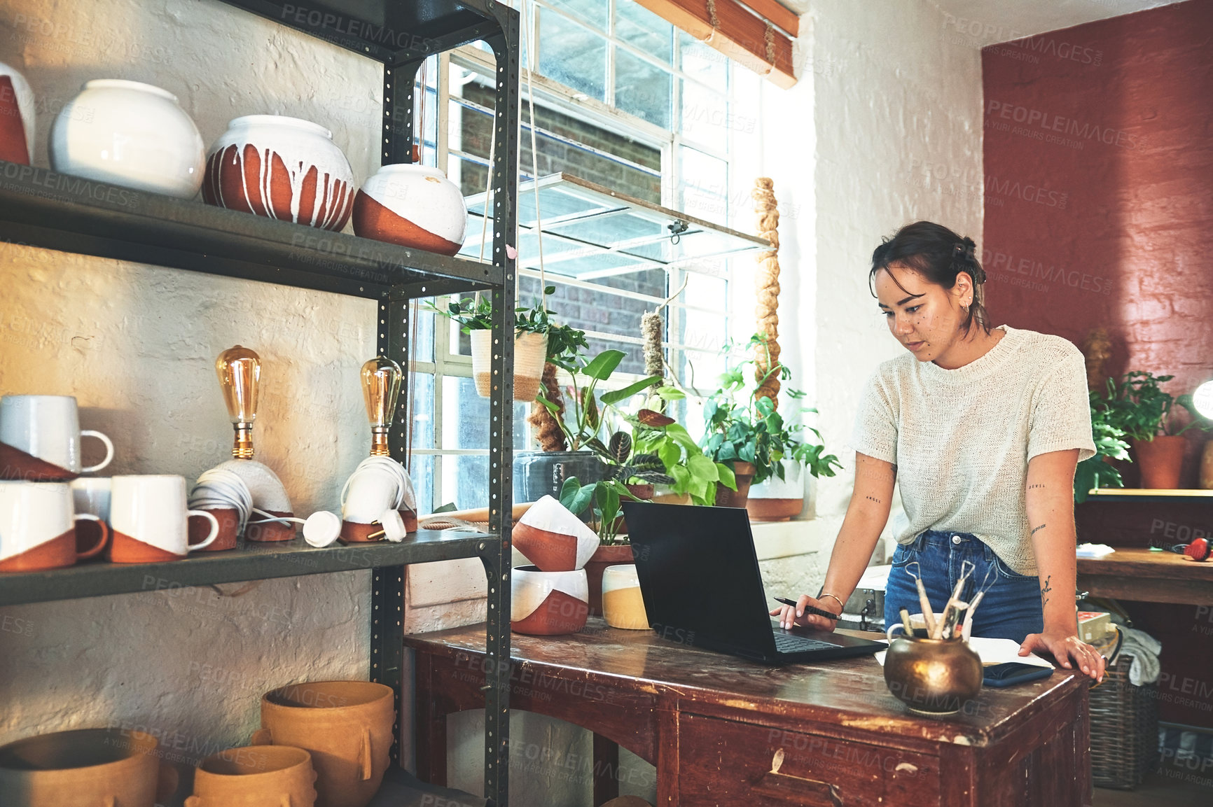 Buy stock photo Cropped shot of an attractive young business owner standing and using her laptop in her pottery studio