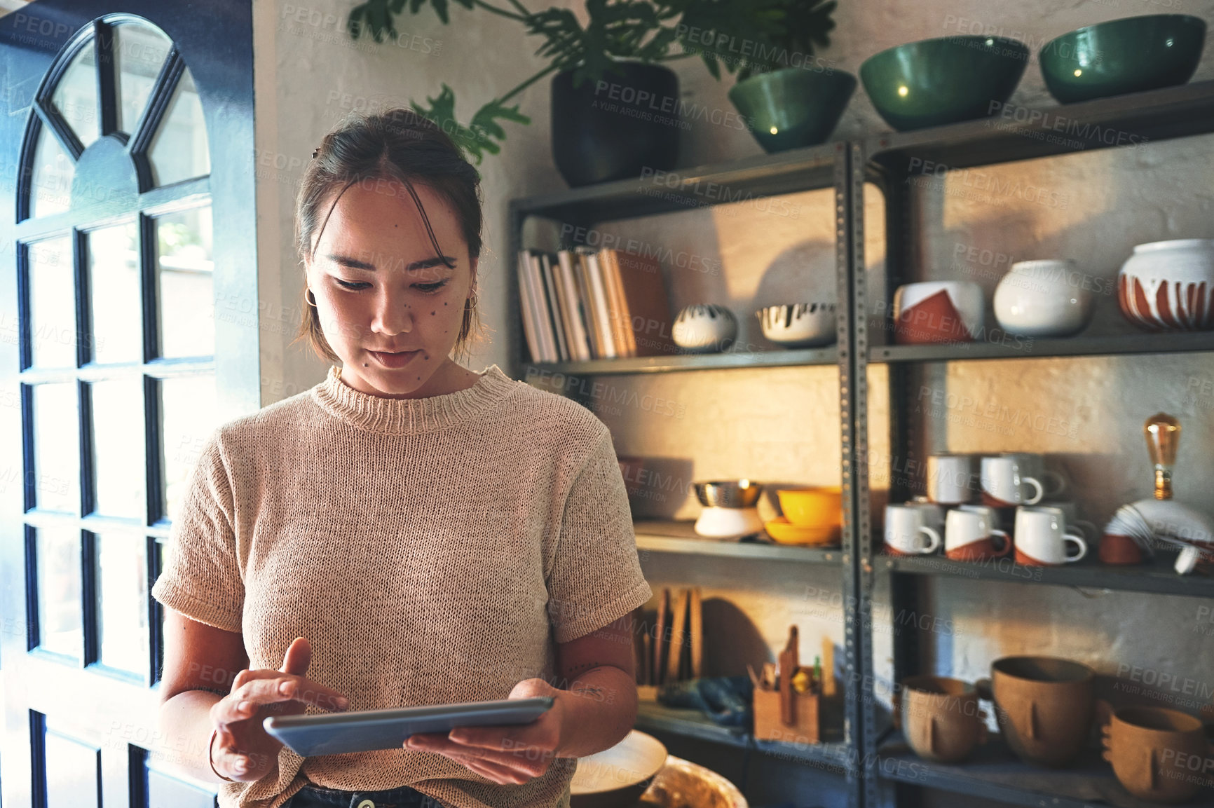 Buy stock photo Cropped shot of an attractive young business owner standing alone in her pottery studio and using a tablet