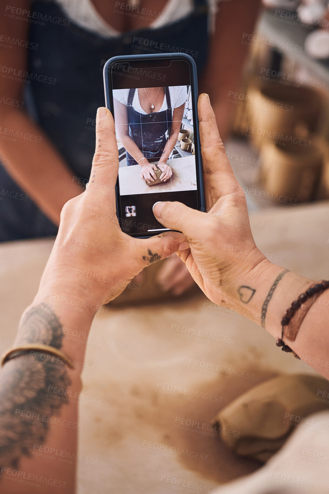 Buy stock photo Shot of a woman using a smartphone to take pictures of her friend in a pottery studio