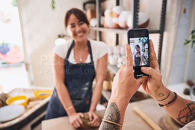 Buy stock photo Shot of a woman using a smartphone to take pictures of her friend in a pottery studio