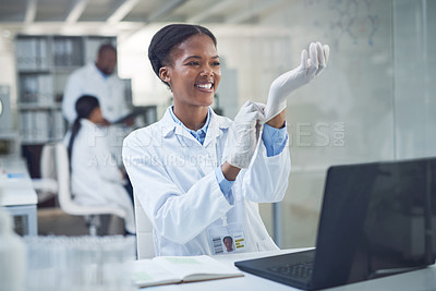 Buy stock photo Shot of a young scientist putting on gloves while conducting research in a laboratory