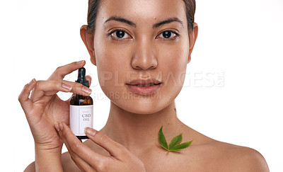 Buy stock photo Shot of a beautiful young woman holding a bottle of CBD oil against a white background