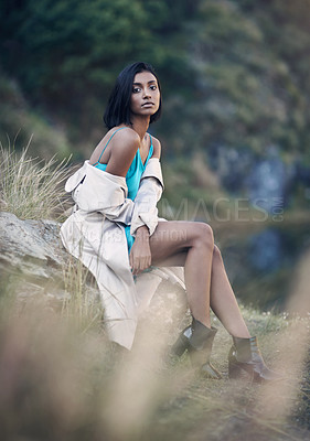 Buy stock photo Shot of a fashionable young woman sitting against a rock outdoors