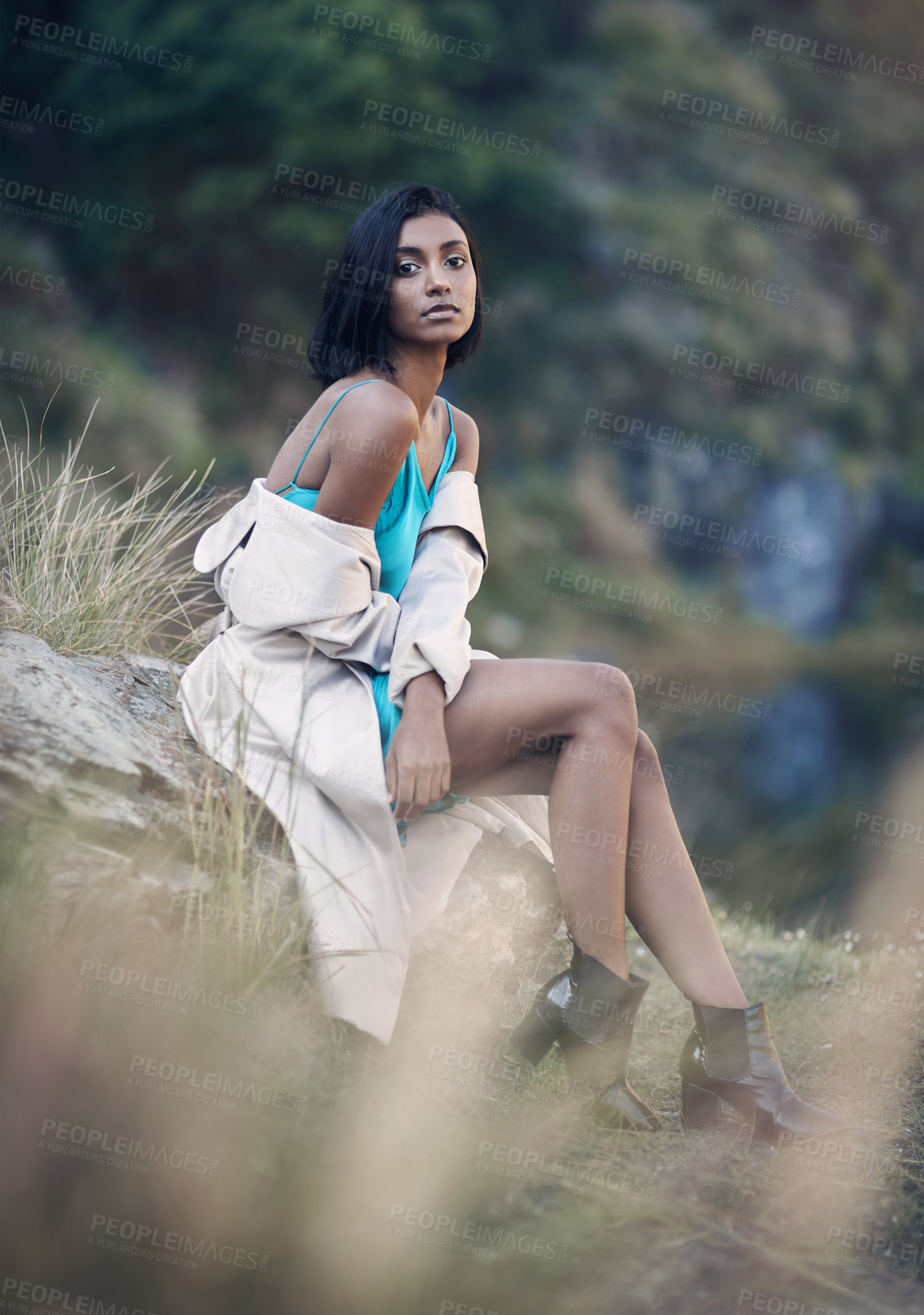 Buy stock photo Shot of a fashionable young woman sitting against a rock outdoors