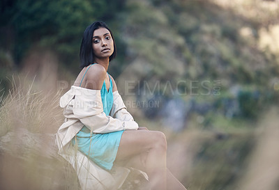 Buy stock photo Shot of a fashionable young woman sitting against a rock outdoors