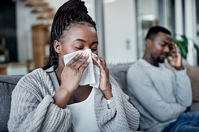 Buy stock photo Young, sick and ill woman blowing her nose with tissues while sitting on the couch at home. African lady has cold or flu and needs medicine. Husband worried about wife suffering from illness 