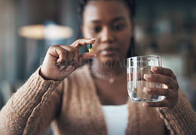 Buy stock photo Cropped shot of an attractive young woman sitting alone and taking her medication with water in her living room