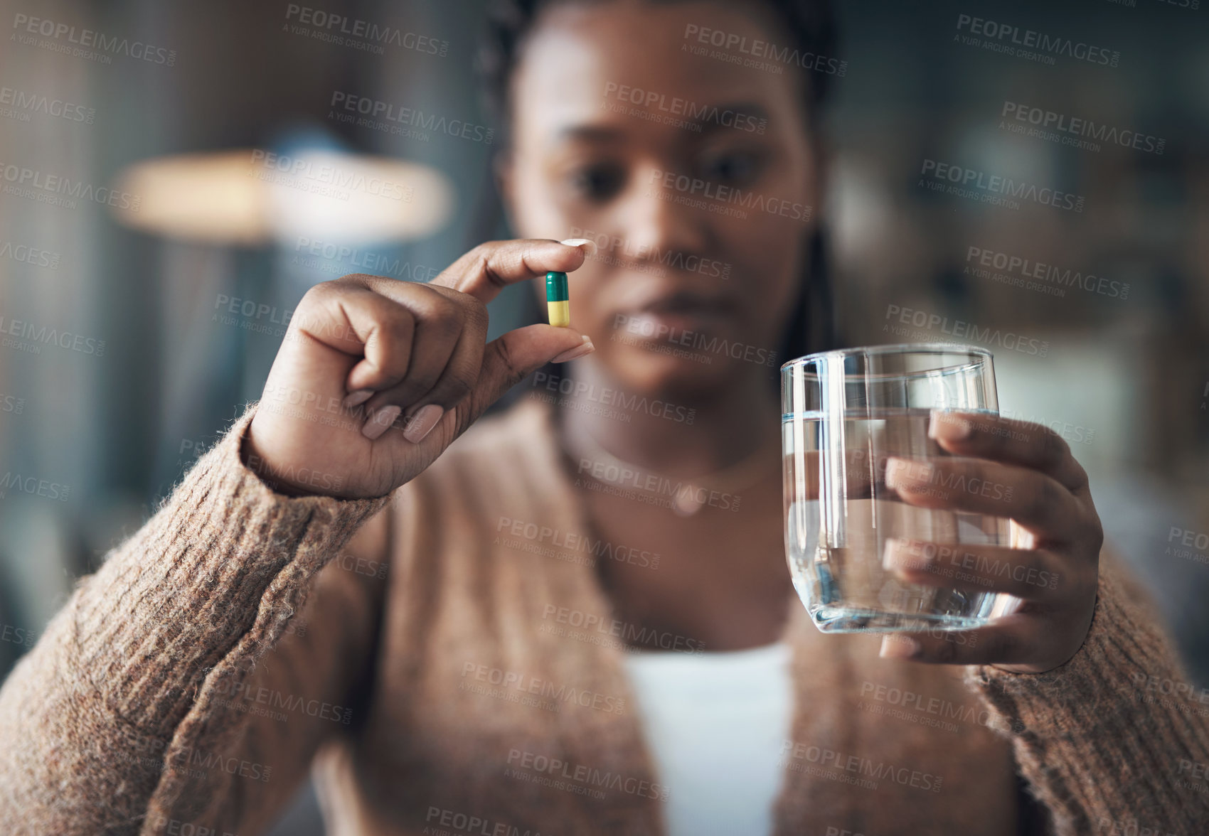 Buy stock photo Cropped shot of an attractive young woman sitting alone and taking her medication with water in her living room