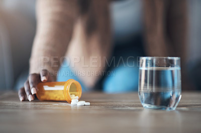 Buy stock photo Cropped shot of an unrecognizable woman sitting alone and taking pills out of a pill bottle in her living room