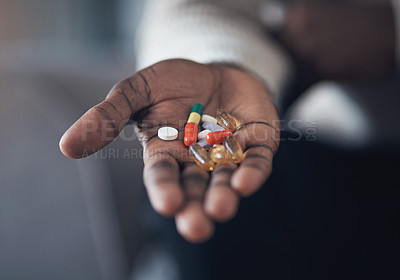 Buy stock photo Cropped shot of an unrecognizable man sitting alone in his living room and holding his medication in his hand