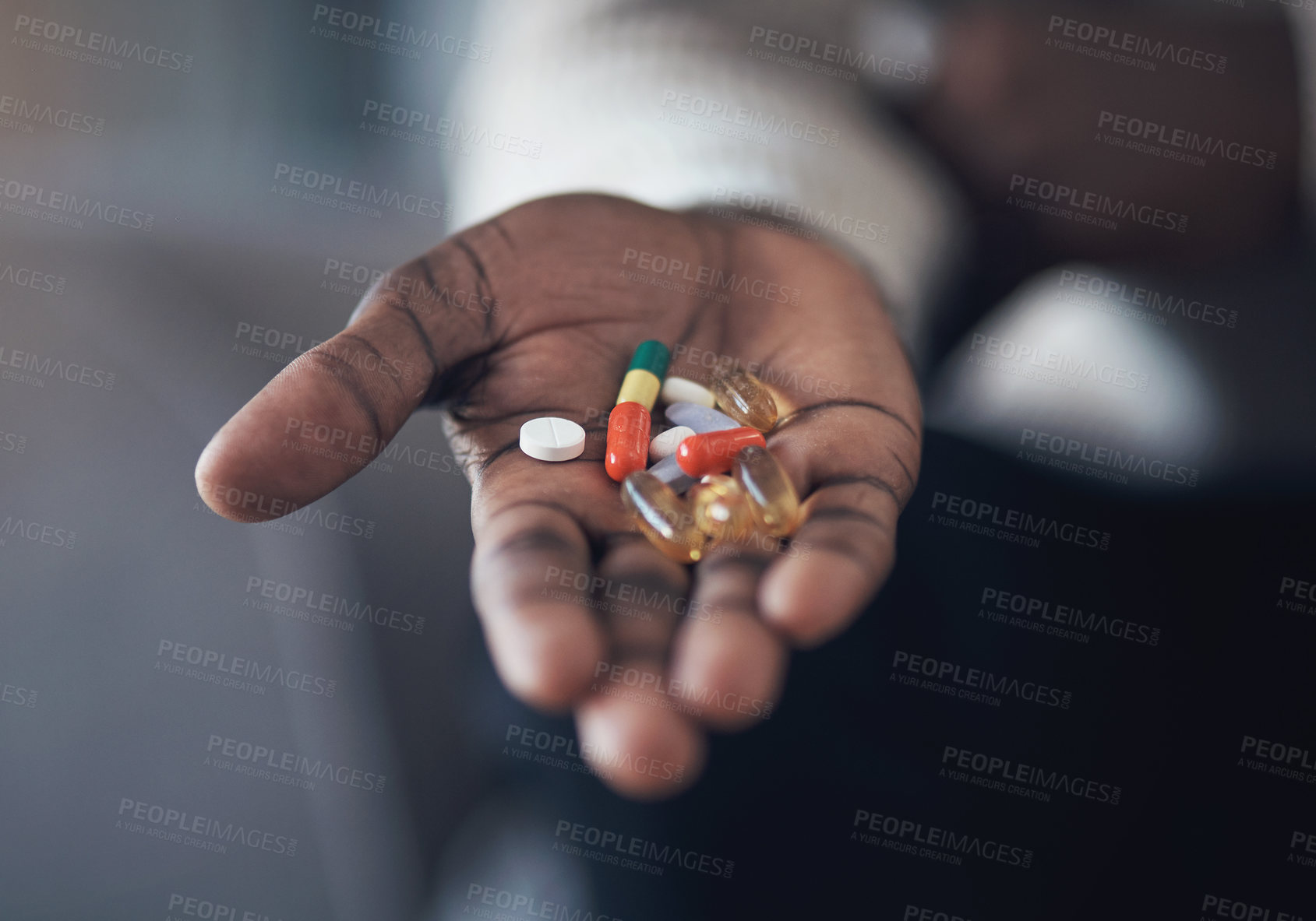 Buy stock photo Cropped shot of an unrecognizable man sitting alone in his living room and holding his medication in his hand