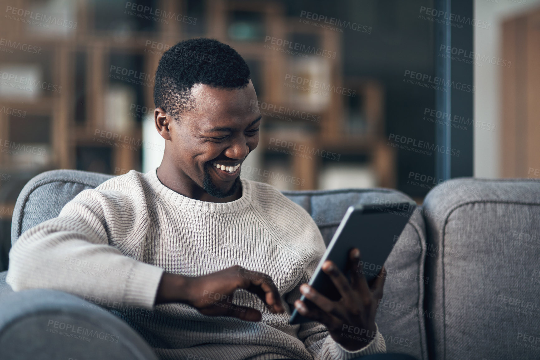 Buy stock photo Cropped shot of a handsome young man sitting alone in his living room and using his tablet