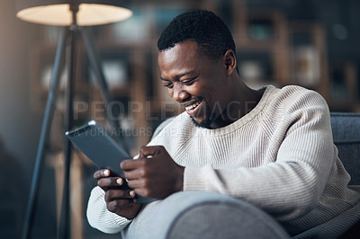 Buy stock photo Cropped shot of a handsome young man sitting alone in his living room and using his tablet
